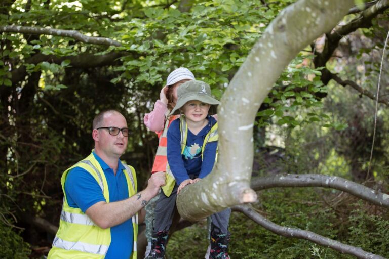 Children Sitting on a Tree Branch in the Forest with Nursery Nurse