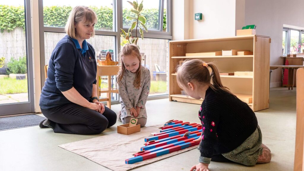 Two children and a nursery nurse playing with Montessori toys in the nursery, fostering hands-on learning.