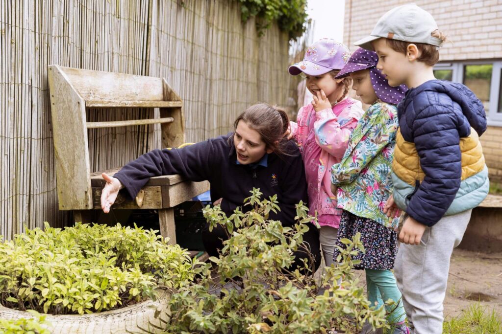 Children participating in an outdoor activity with a nursery nurse, learning about plants.