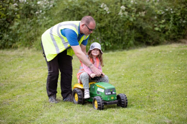 Nursery Nurse Helping a Child Ride a Toy Tractor in the Garden