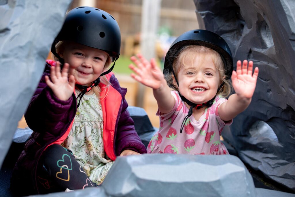 Smiling children waving while wearing safety helmets